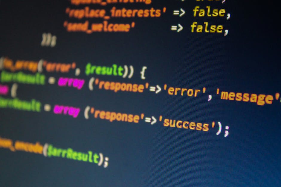 Close-up of a computer screen displaying lines of programming code with syntax highlighting in various colours, including green, purple, yellow, and orange. The background of the screen is black, and 